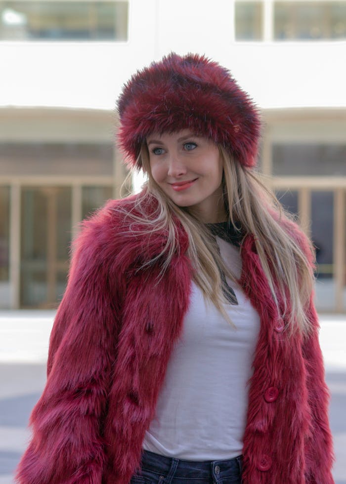 rusia-girl-19328522 Stylish woman wearing a red fur hat and coat, casually standing in a city environment.